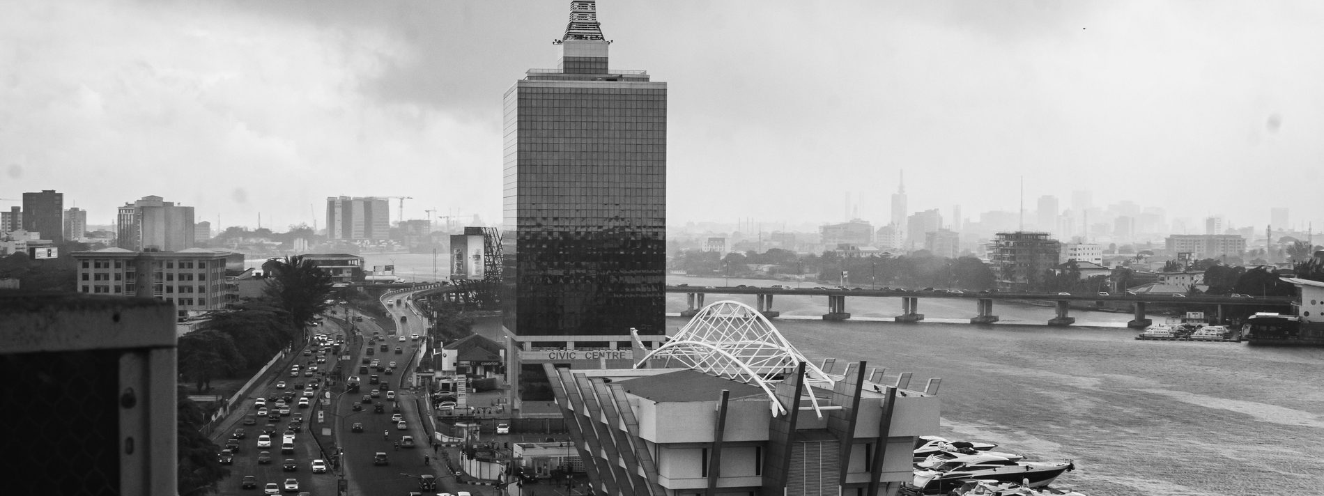 The Lagos waterfront on Victoria Island: the Civic Centre tower above traffic on Ozumba Mbadiwe Avenue, with Falomo Bridge crossing the lagoon behind